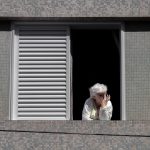Older woman looking out from a window in a quiet home, reflecting during a life transition.
