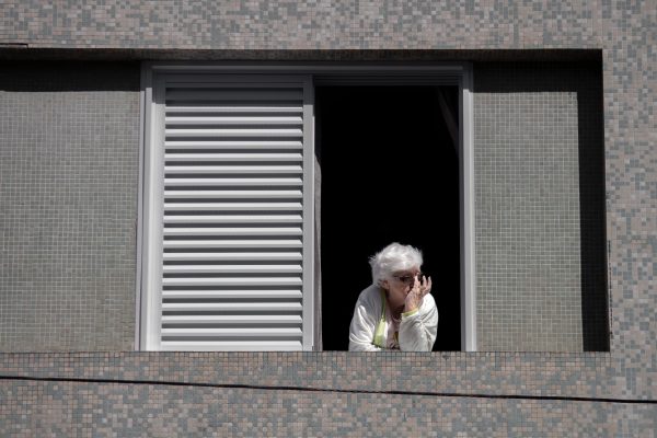 Older woman looking out from a window in a quiet home, reflecting during a life transition.