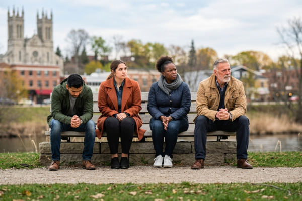 Four diverse adults sitting thoughtfully on a park bench representing the community need for mental health support in Guelph.